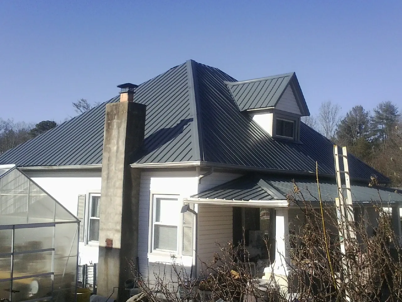 Dark blue standing seam metal roof on a white farmhouse with dormer — Slate & Tile Roof Repair by Roofing Brothers in Jasonville
