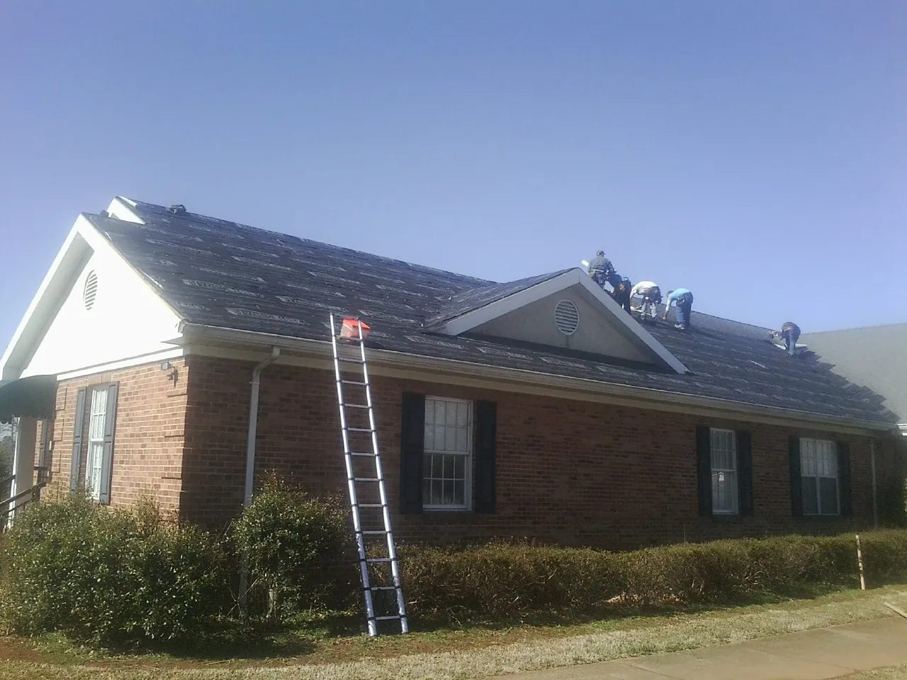 Crew tearing shingles off a brick ranch roof with a ladder set — Emergency Roof Repair work by our crew in Jasonville