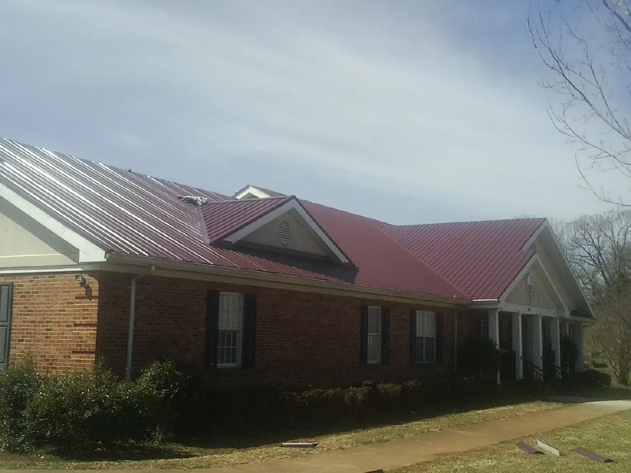 Red metal roof with gabled entries on a long brick building, from a Hail Damage Roof Repair job in Jasonville