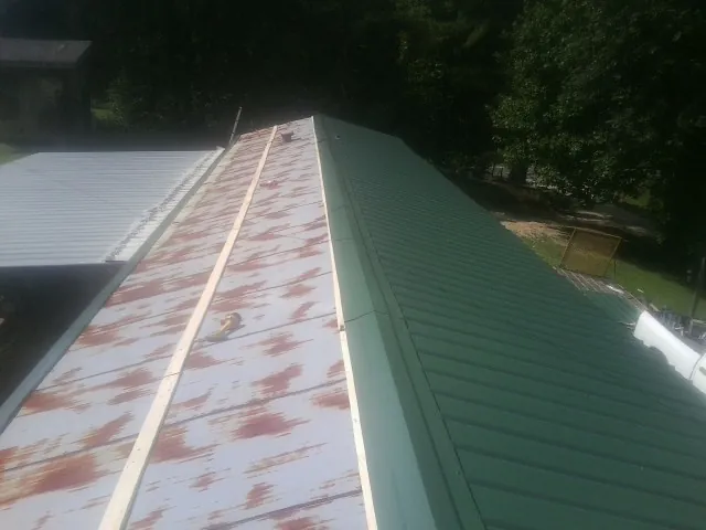 Old rusted panels beside newly installed green metal roofing — Wind Damage Roof Repair by Roofing Brothers in Jasonville