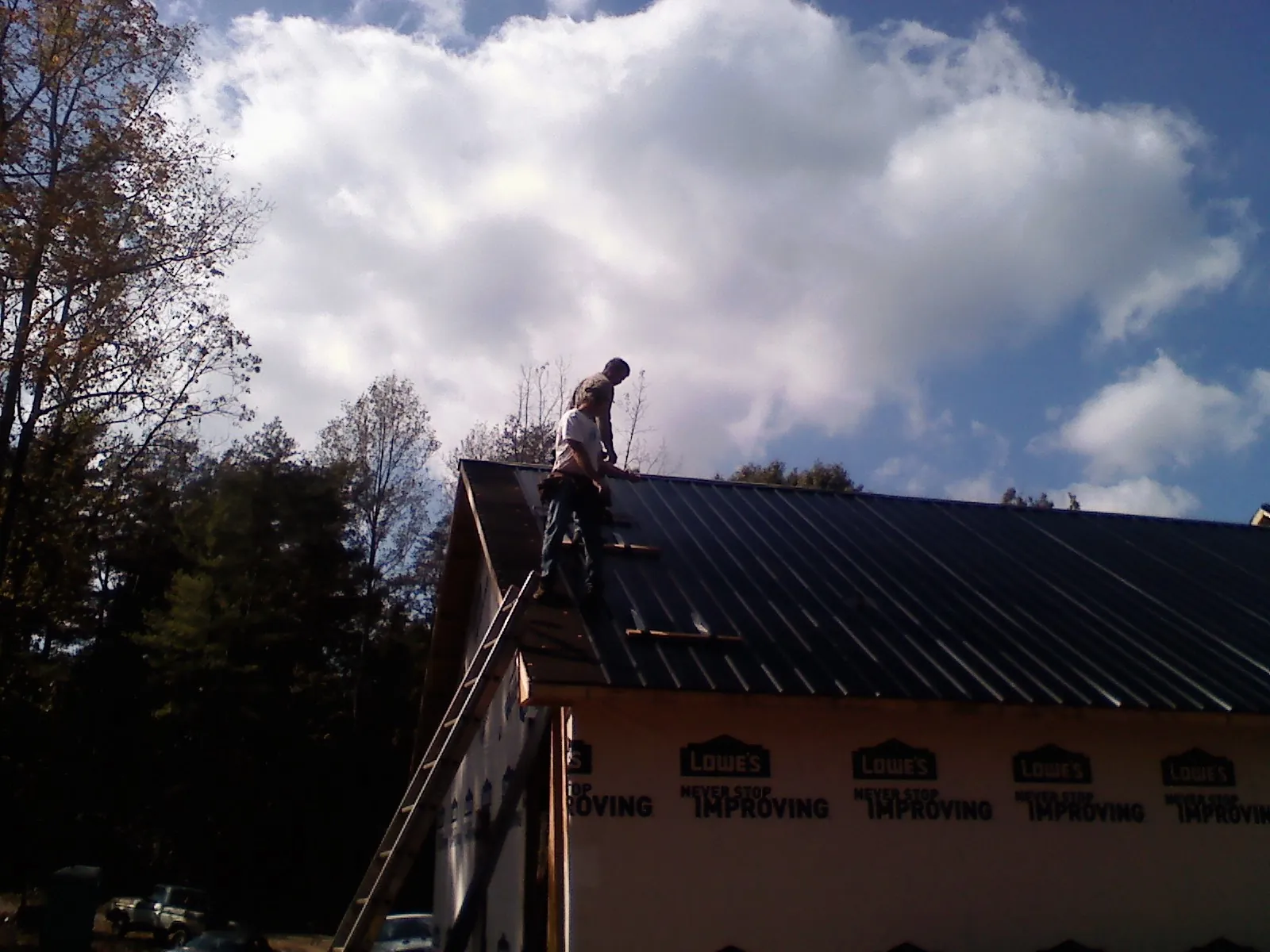 Roofer fastening dark metal panels high against a cloudy sky, from a Roof Inspection job in Jasonville