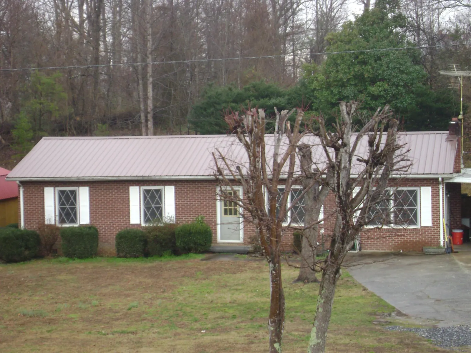 Mauve metal roof on a brick ranch home behind bare trees in Jasonville