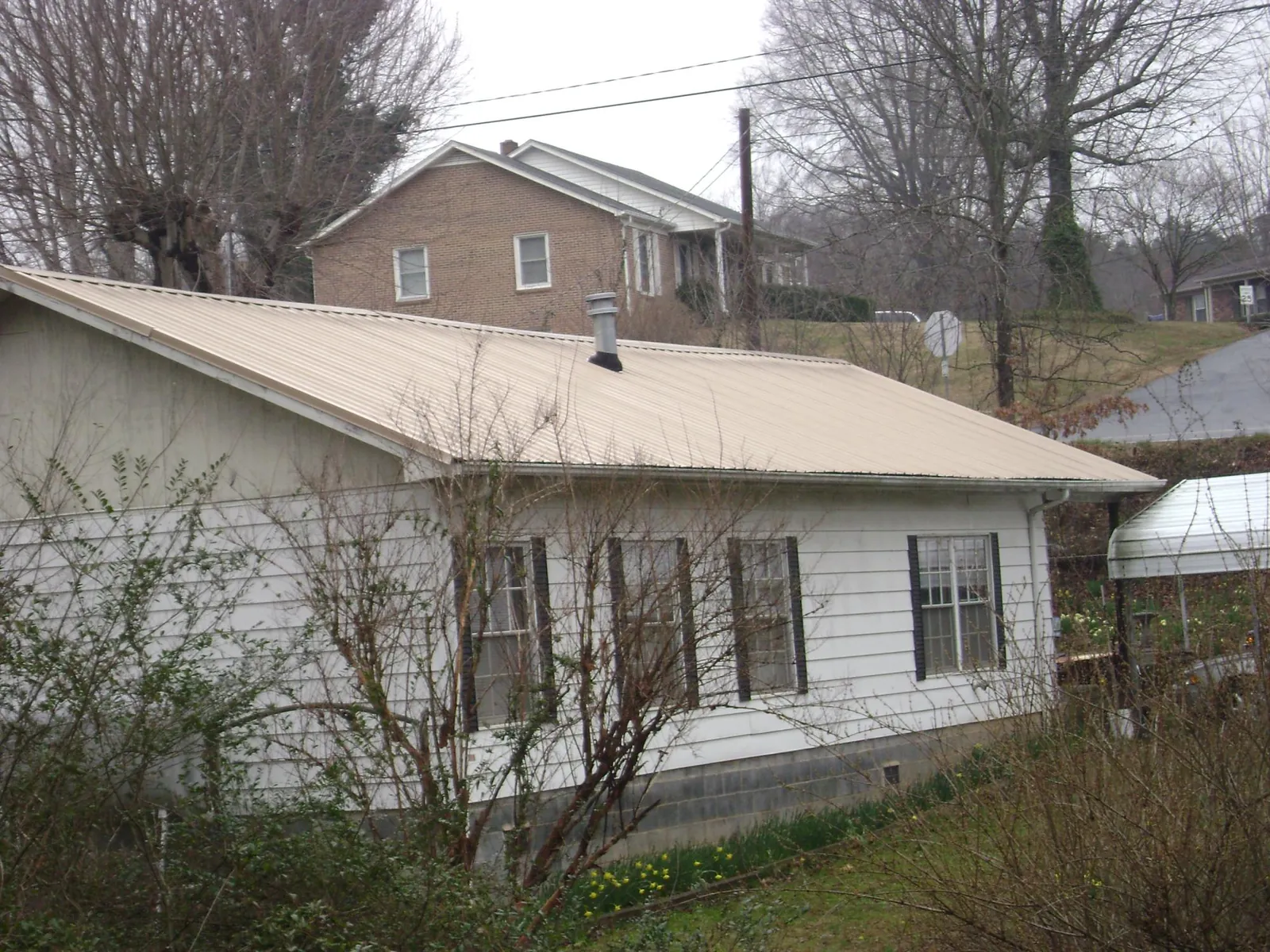 Tan metal roof on a white sided house set into a hillside — Commercial Roofing by Roofing Brothers in Jasonville