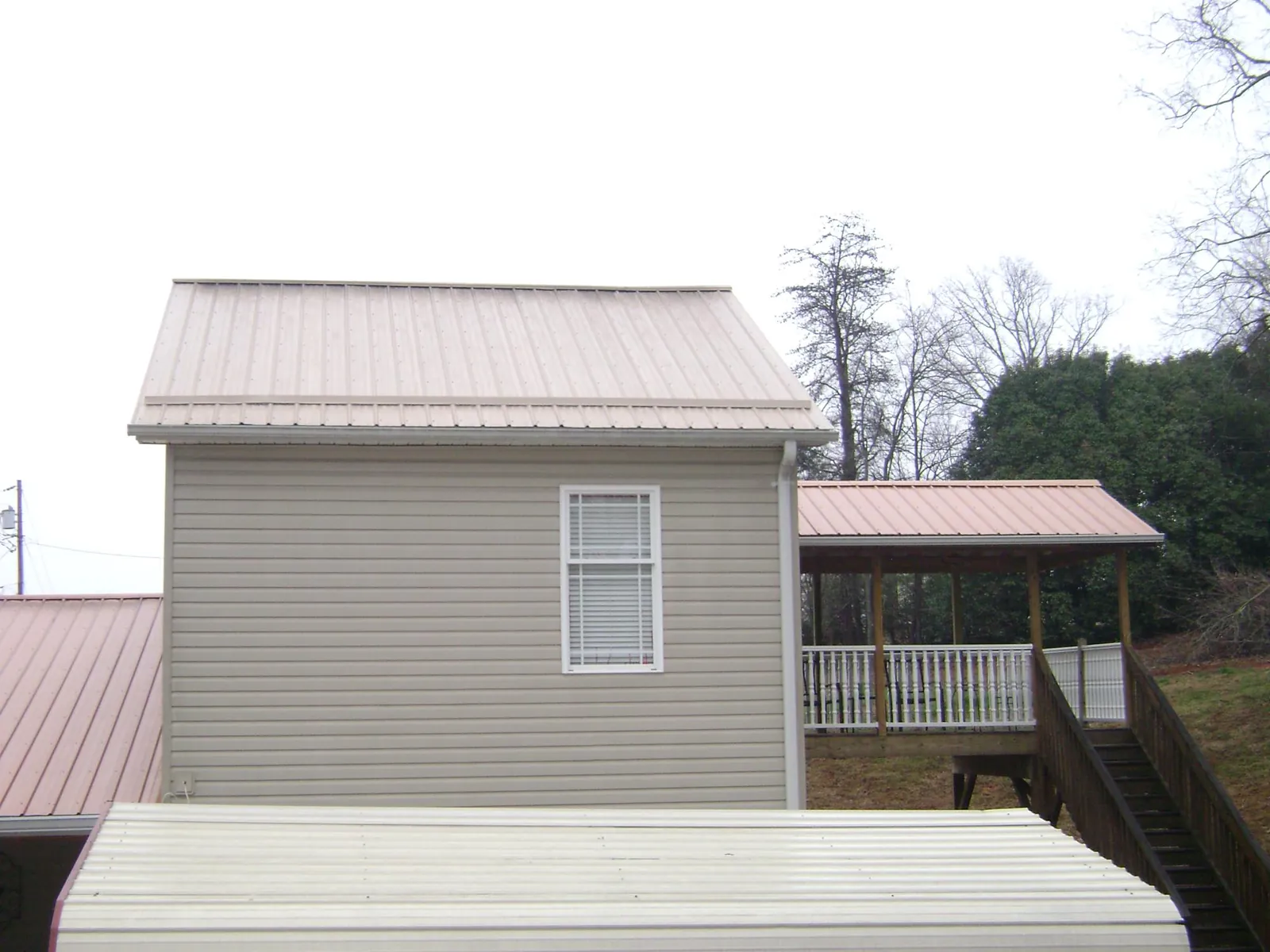 Tan metal roofs on a two story addition and attached porch, from a Roof Replacement job in Jasonville